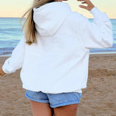 Person wearing a white hoodie and denim shorts on a beach